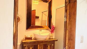 A bathroom with a wooden vanity, a white sink, a mirror, and a hanging light fixture.