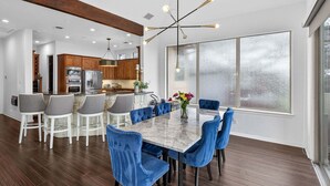 A modern kitchen with wooden cabinets, a marble island, and a dining area with blue chairs and a marble table.