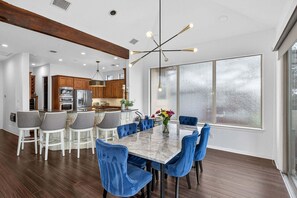 A modern kitchen with wooden cabinets, a marble island, and a dining area with blue chairs and a marble table.