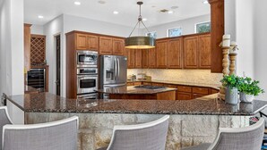 A kitchen with granite countertops, wooden cabinets, stainless steel appliances, and a central island with bar seating.