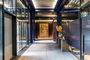 A modern hotel lobby with a glass wall, a reception desk, and a large poster on the wall. - Luxury Mayfair 3-bed AC Parking Gym Security (London)