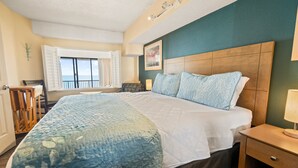 Une chambre d’hôtel avec un grand lit, une tête de lit en bois, une table de chevet, une fenêtre avec des rideaux et une vue sur la mer.