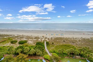 A beach view with a pathway leading to a building, a sandy beach, and some greenery. - 1BR Oceanfront on the Golden Mile (Myrtle Beach)