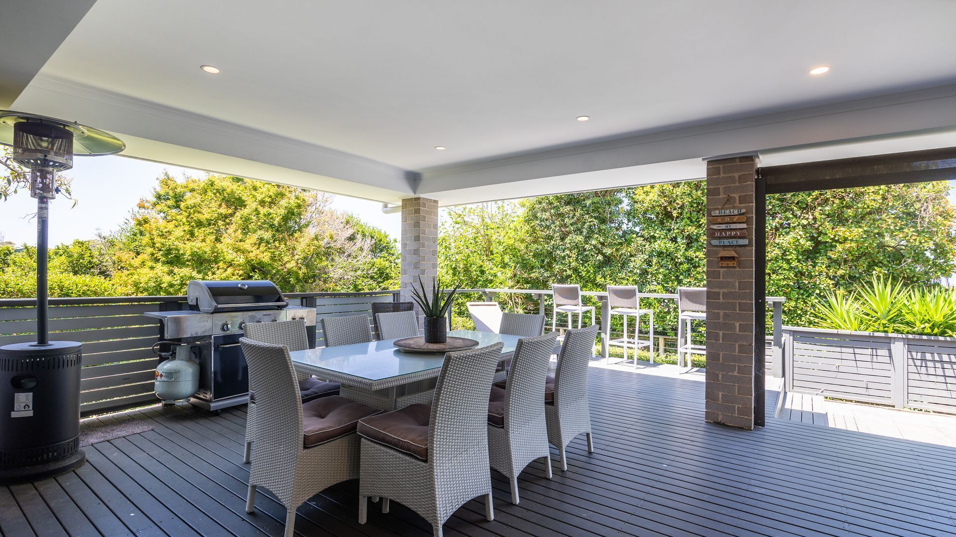 An outdoor patio with a grill, wicker furniture, and a view of greenery.