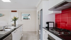 A modern kitchen with a gas stove, stainless steel appliances, and a red backsplash. - Molly-Wallee a walk to the beach (Mollymook Beach)