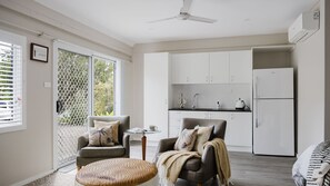 A modern kitchen with white cabinets, a refrigerator, and a dining area with a table and chairs. - Molly-Wallee a walk to the beach (Mollymook Beach)