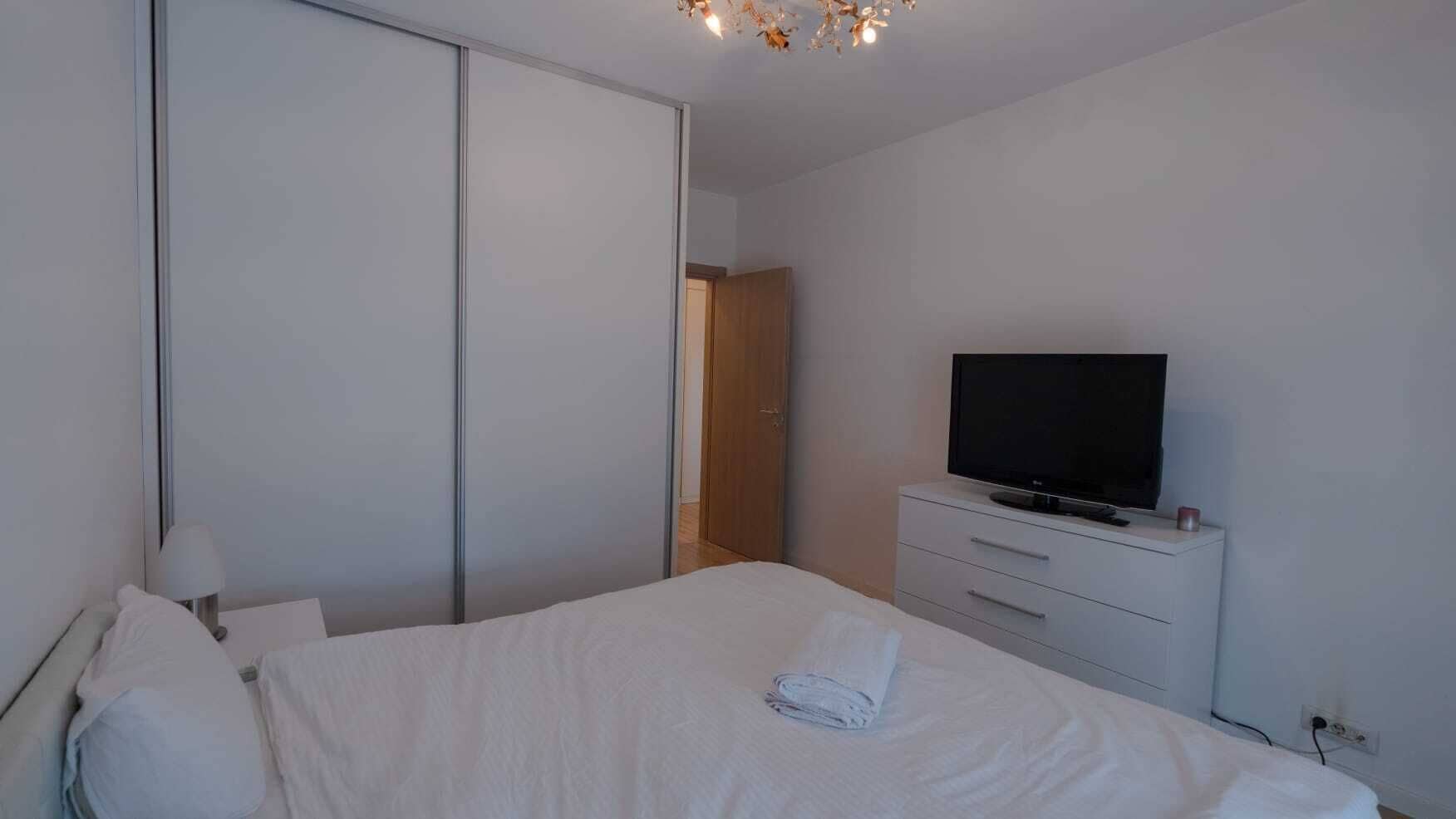 A bedroom with a bed, a television on a dresser, and a wardrobe.