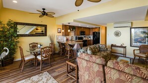 A spacious living area with a dining set, a sofa, and a ceiling fan. - Kona Alii 711 - Oceanfront Kona Penthouse w/ AC | Walk to Town (Kailua Kona)
