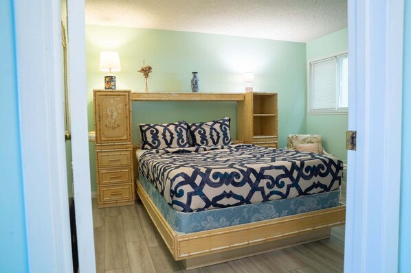 A bedroom with a bed, a nightstand, a dresser, and a window. - Banyan Tree 304 - Oceanfront Kona Condo w/ Views, Pool & Lanai (Kailua Kona)