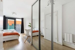 Ein modernes Schlafzimmer mit Bett, Sessel, einer Tür und Blick durch eine Glastür.