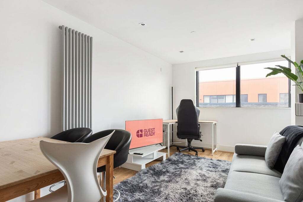 A modern room with a desk, chair, sofa, and a 'GUEST READY' sign.