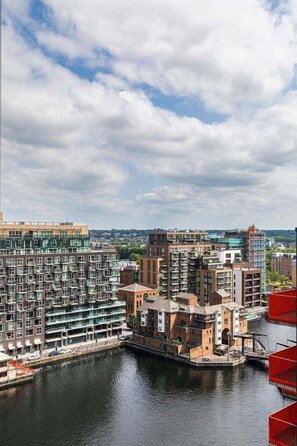 A riverside view of modern buildings with a dock and a red structure. - GuestReady – Stylish urban retreat in Canary Wharf (London)