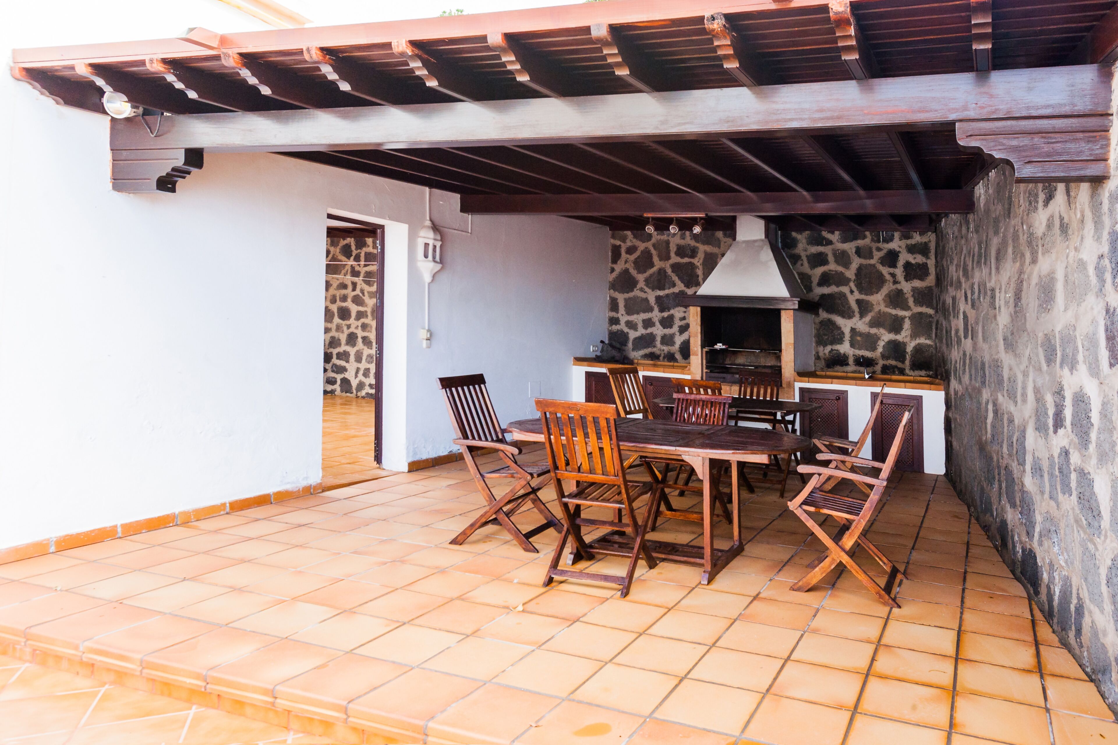 Une terrasse extérieure avec un mur en pierre, un barbecue et des meubles en bois.