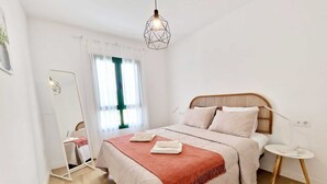 Une chambre à coucher avec un lit, des tables de chevet, un luminaire suspendu et une fenêtre avec des rideaux.