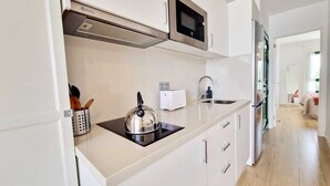 Une cuisine moderne avec des meubles blancs, une bouilloire en acier inoxydable, un four à micro-ondes et un grille-pain.