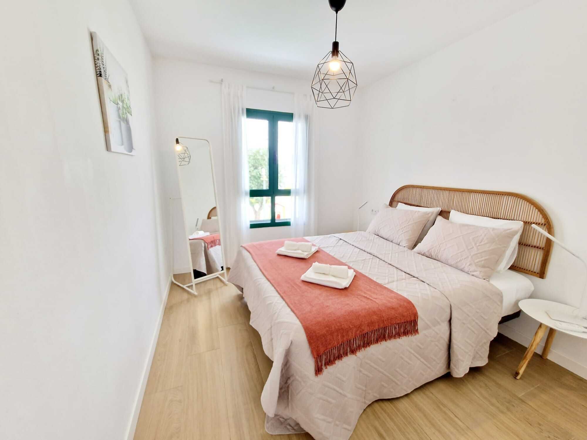 Ein Schlafzimmer mit Bett, Nachttisch, Spiegel und einer Pendelleuchte.