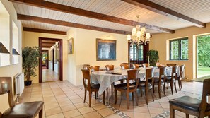 A dining area with a large table, chairs, and a chandelier. There is a hallway leading to another room.