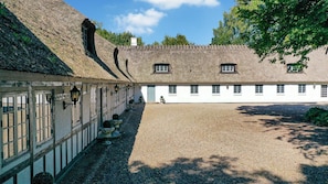 A courtyard with a building featuring a thatched roof and white walls, surrounded by gravel. - VillaVilla 951 - Nr. Aaby, Fyn og øer (Nørre Aaby)