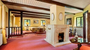 A spacious room with a fireplace, a dining table with chairs, and a large window.