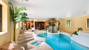 Een binnenzwembad met een jacuzzi, een trap naar een hoger niveau, en een tropische plant.