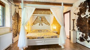 Een hemelbed met een bloemenbedekking, een wandlamp en een groot dierenhuid aan de muur.