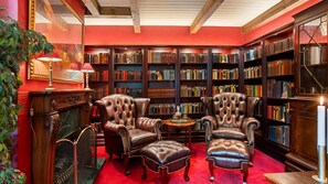 Una biblioteca con sillones de cuero, una chimenea y estanterías llenas de libros.
