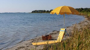 Een strand met een gestreepte ligstoel, een gele paraplu met stippen en een rieten mand.