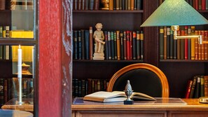 Eine Bibliothek mit Bücherregalen, einer Statue, einem offenen Buch und einem Schreibtisch mit einer Lampe.