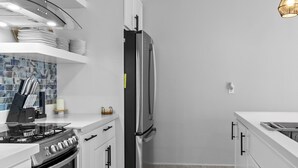 Une cuisine moderne avec des meubles blancs, des appareils électroménagers en acier inoxydable, une cuisinière à gaz et un sol en marbre.