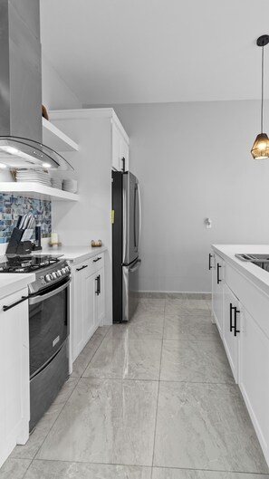 A modern kitchen with white cabinetry, stainless steel appliances, a gas stove, and a marble floor. - NEW! Oceanfront Casita w/ Private Plunge Pool, Ocean Access w/ Dock & Concierge (Punta Blanca)