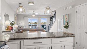 A kitchen with granite countertops, white cabinets, a ceiling fan, pendant lights, and a view to the outside. - New! Bayfront Condo w/ 2 Balconies, Loft & Pool – Walk to Beach (Fort Walton Beach)