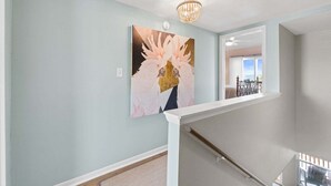 A staircase with a white handrail, a chandelier, and a painting of birds on the wall. - New! Bayfront Condo w/ 2 Balconies, Loft & Pool – Walk to Beach (Fort Walton Beach)