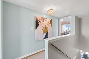 A staircase with a white handrail, a chandelier, and a painting of birds on the wall. - New! Bayfront Condo w/ 2 Balconies, Loft & Pool – Walk to Beach (Fort Walton Beach)