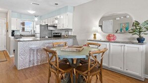 A kitchen with white cabinets, a marble island, wooden chairs, and a round dining table. - New! Bayfront Condo w/ 2 Balconies, Loft & Pool – Walk to Beach (Fort Walton Beach)
