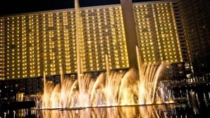 Ein großes Hotel mit einheitlicher Fassade aus beleuchteten Fenstern, einer zentralen vertikalen Struktur und einer Wasserspielen im Vordergrund.