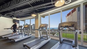 Ein Fitnessstudio mit Laufbändern und einer Person, die eines benutzt, großen Fenstern und Blick auf ein Gebäude im Freien.