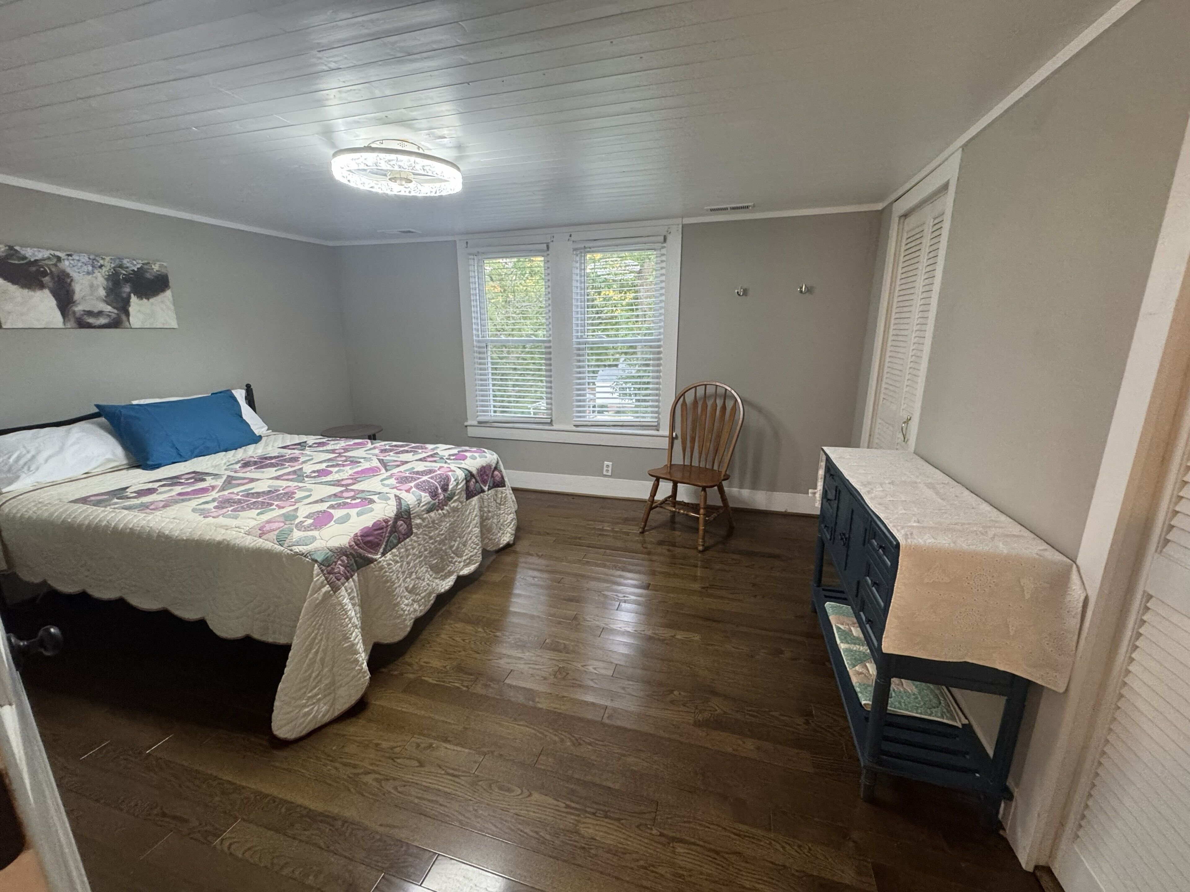 Une chambre à coucher comprenant un lit, une chaise, une commode et une fenêtre avec des stores.