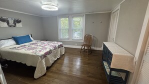 Une chambre à coucher comprenant un lit, une chaise, une commode et une fenêtre avec des stores.