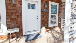 En træfacade med to hvide døre, en bænk og et skilt med teksten 'Captains Quarters'.