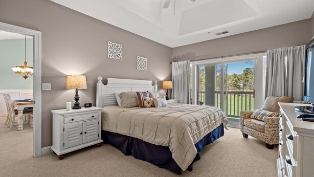 A bedroom with a bed, bedside tables, a chair, a ceiling fan, and a view of the outdoors. - Stylish Myrtle Beach Retreat, Golf Views • Pool • Near Beach and Broadway (Myrtle Beach)