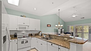 A kitchen with white cabinets, a granite countertop, a microwave, an oven, a dishwasher, and a ceiling fan. - Stylish Myrtle Beach Retreat, Golf Views • Pool • Near Beach and Broadway (Myrtle Beach)