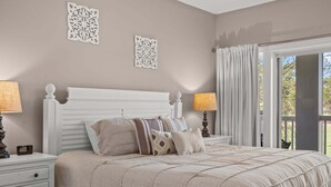 A bedroom with a bed, nightstands, decorative wall pieces, and a view through a window. - Stylish Myrtle Beach Retreat, Golf Views • Pool • Near Beach and Broadway (Myrtle Beach)