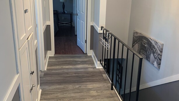 Un couloir avec un plancher en bois, des portes blanches et une rambarde noire.