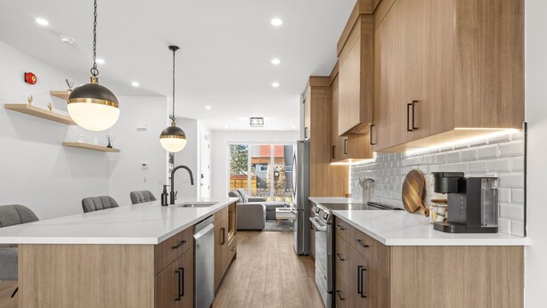 Une cuisine moderne avec des meubles en bois, un îlot central, des luminaires suspendus et une vue sur l’espace de vie.