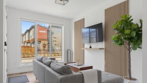 Un salon moderne avec un canapé gris, un téléviseur à écran plat, un mur recouvert de lambris en bois et une plante en pot.