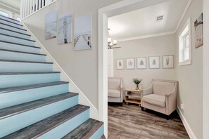 A staircase with blue steps leading to a landing, a beige armchair, a small table with a vase, and framed botanical prints on the wall. - Charming Boho Retreat Located on Tybee's South End | Heated Pool Access (Tybee Island)