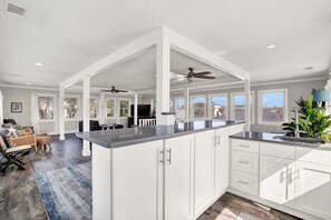 A spacious kitchen with white cabinetry, a large island, and a view of the outdoors. - Charming Boho Retreat Located on Tybee's South End | Heated Pool Access (Tybee Island)