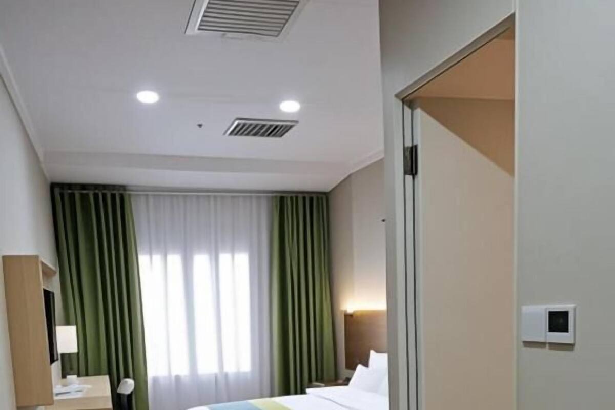 A hotel room with a bed, a desk, a chair, a suitcase, and a door.
