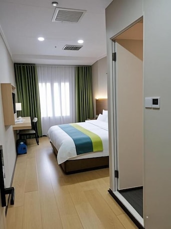 A hotel room with a bed, a desk, a chair, a suitcase, and a door.