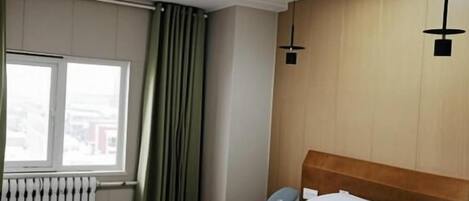 A hotel room with a bed, a window with curtains, a radiator, and a ceiling vent.